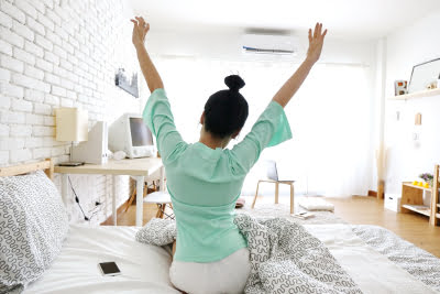 woman sits on a bed with air conditioning unit in the background