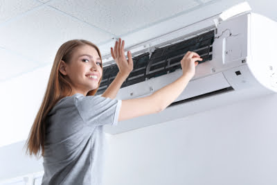 Smiling woman stands next to a wall mounted air conditioning unit