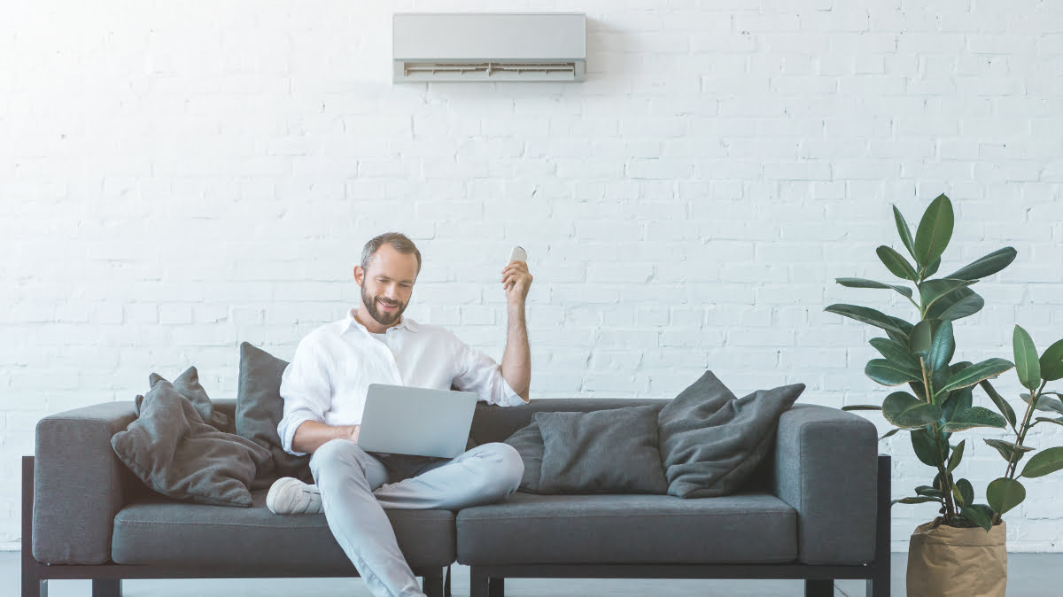 Man adjusts his air conditioning with a remote control while sitting on a sofa