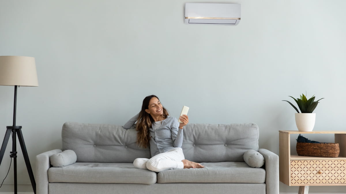 Woman sits on a sofa in a flat and controls her air conditoning