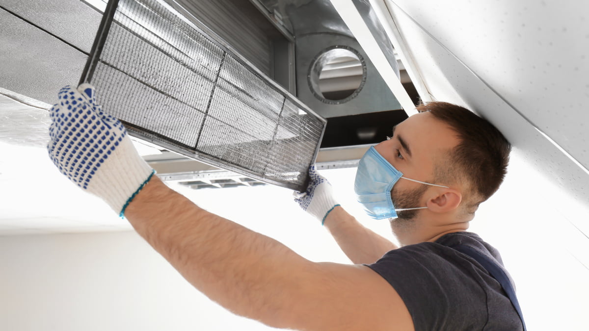 air conditioning engineer removing unit panel wearing face mask