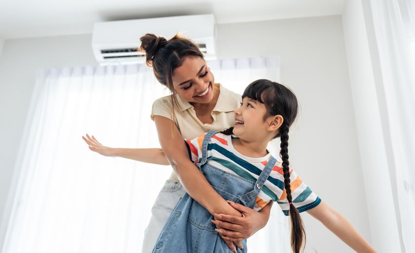 Happy mother and daughter playing in house beneath air con unit