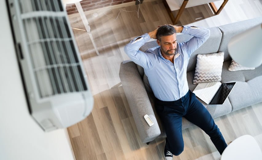 Man relaxing on sofa underneath a wall mounted air con unit